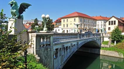 Eine Steinbrücke führt über einen Fluss. Die Brücke ist an ihren Enden mit vier Drachen aus Kupferblech dekoriert. Auf der rechten Uferseite des Bildes sieht man Häuser.