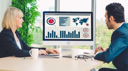 Zwei Personen sitzen vor einem Bildschirm und besprechen Daten, Grafiken, Statistiken miteinander